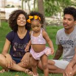 Young family enjoying quality time outdoors, sitting on grass in a park.
