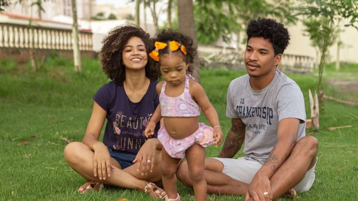 Young family enjoying quality time outdoors, sitting on grass in a park.